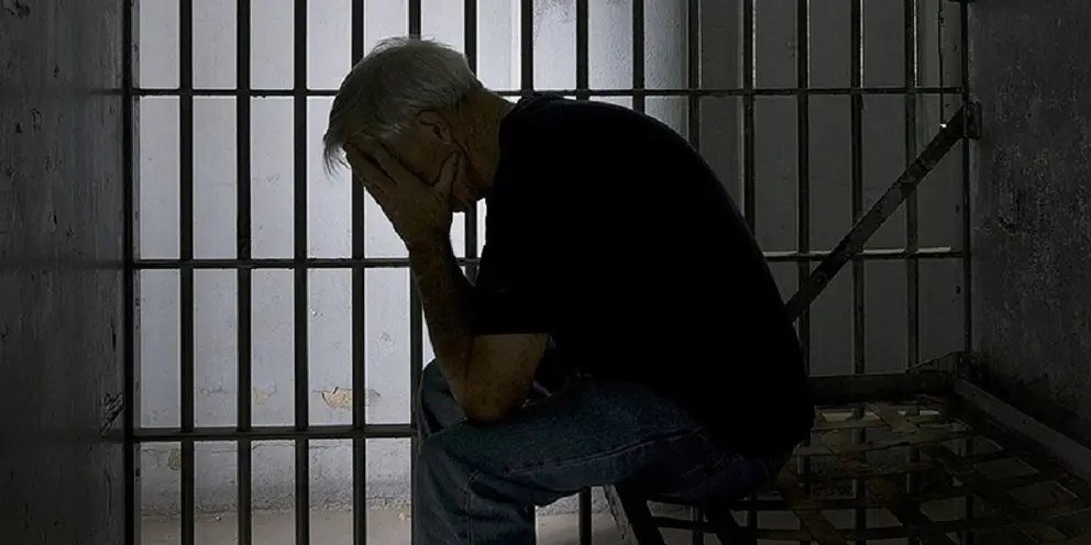 Prisoner in old jail cell with cell bars.