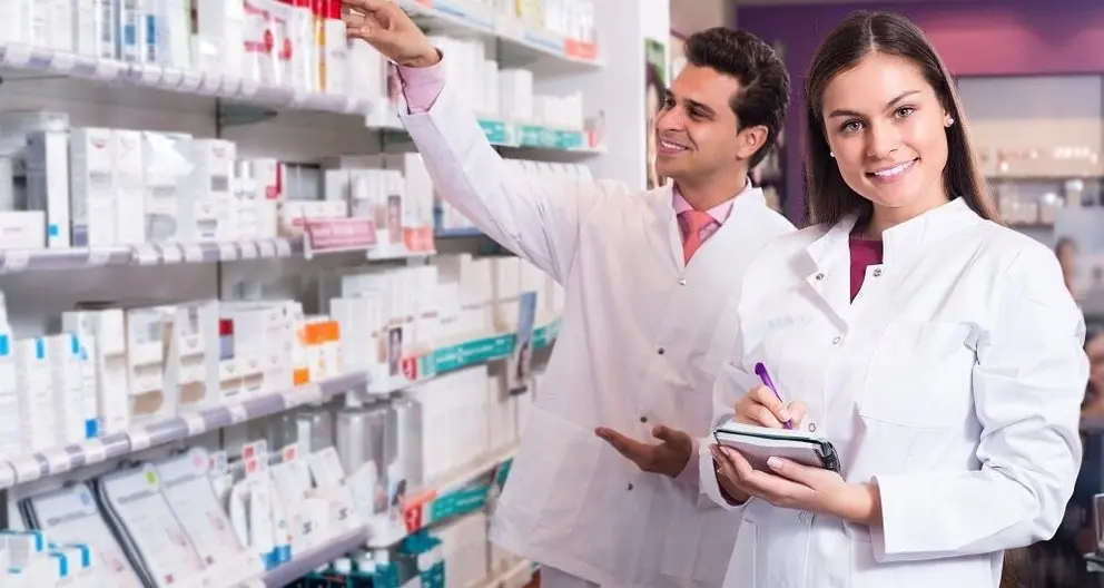 Portrait of two friendly smiling pharmacists in uniform working in modern pharmacy