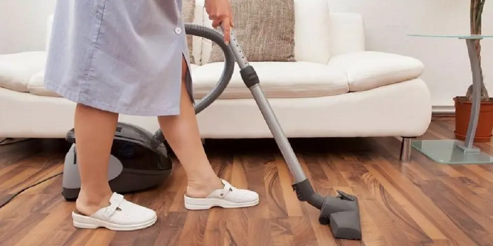 Young Maid Cleaning Floor With Handheld Vacuum Cleaner