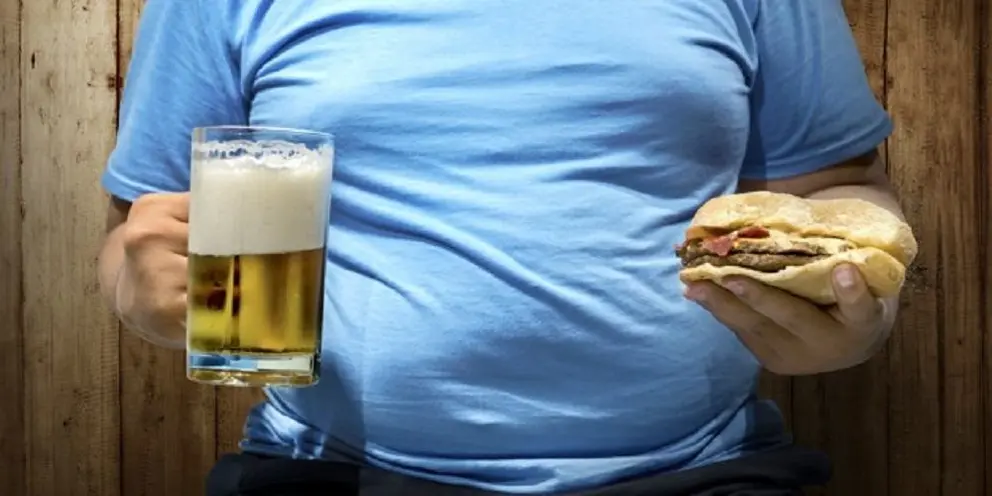 Fat man with beers and hamburger on his hand over wooden wall background