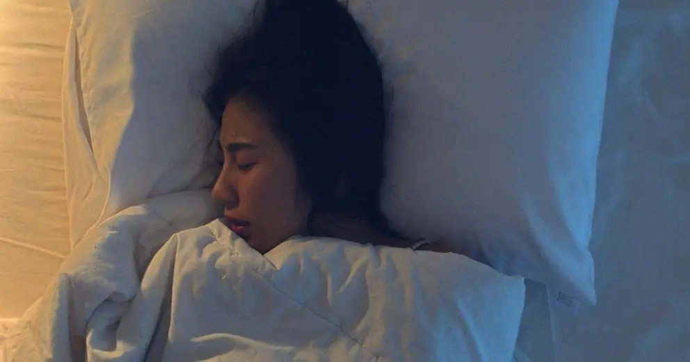 Nervous young Asian woman having a nightmare lying on bed in her bedroom at home in middle of night. Suffering from headache or migraine, Insomnia, sleep apnea or stress concept. Top view shot.