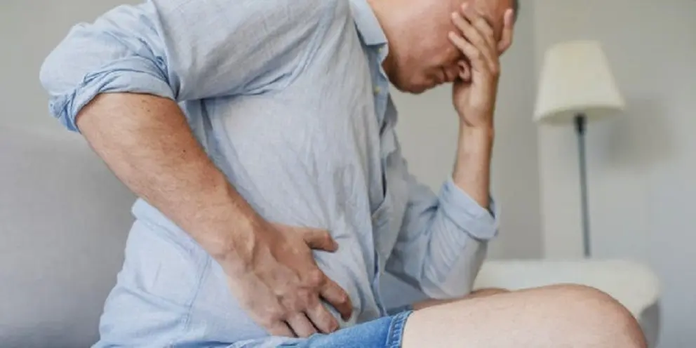 Terrible stomachache. Frustrated handsome young man hugging his belly and keeping eyes closed. Disturbed male having pain in stomach