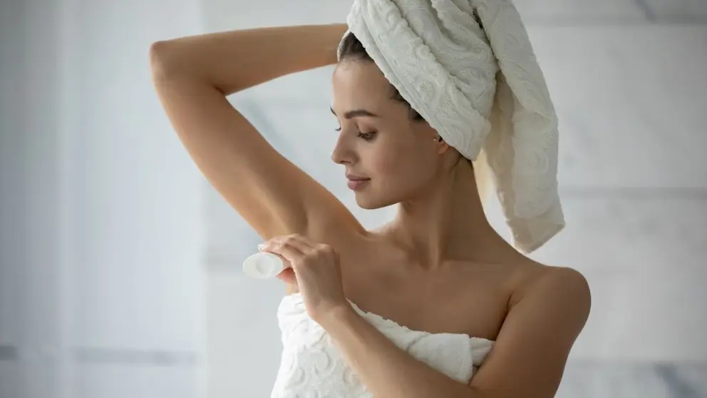 Una mujer aplicando desodorante en las axilas