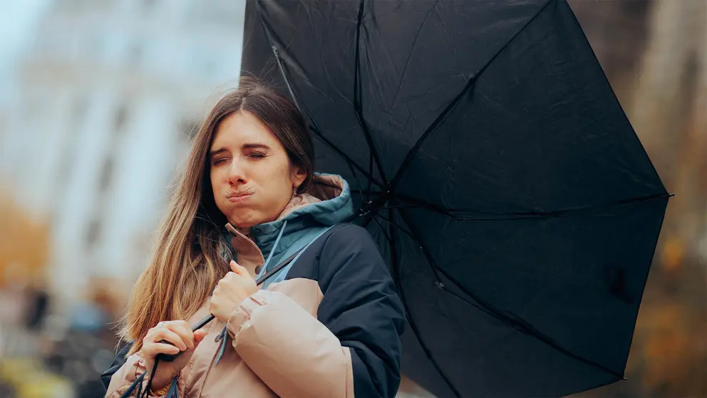 El fuerte viento dobla un paraguas ante la desesperaci&oacute;n de la viandante