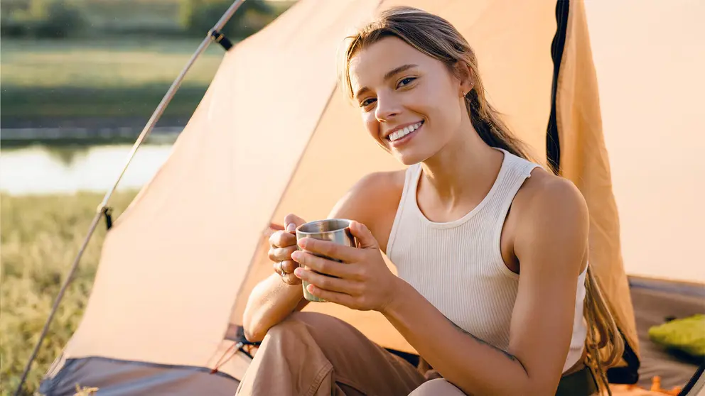 Mujer joven de acampada bebiendo un vaso de agua
