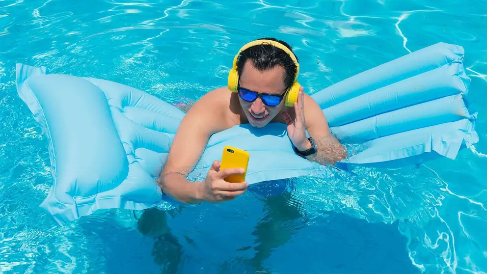 Joven escucha m&uacute;sica dentro de la piscina apoyado en un flotador
