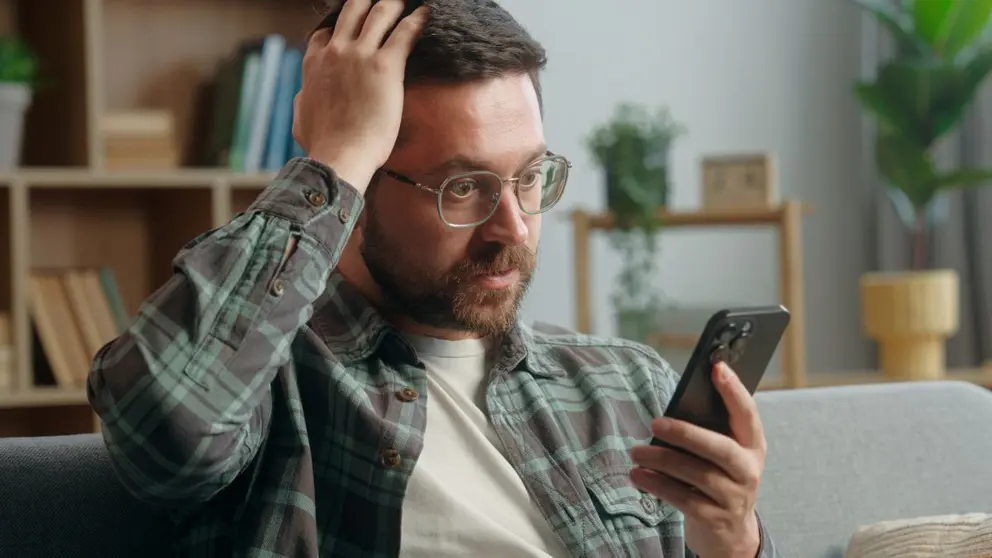 Hombre mira las noticias en su m&oacute;vil con aspecto preocupado