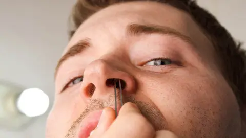 Man pucking nose hair with tweezers while facing camera