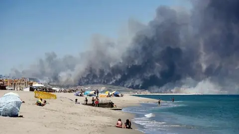 Beach goes sunbath as smoke from forest fire rises above Levante de La Linea beach in the southern Spanish region of Cadiz  Andalusia  on July 12  2016    AFP PHOTO   Marcos Moreno