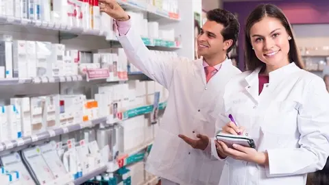 Portrait of two friendly smiling pharmacists in uniform working in modern pharmacy