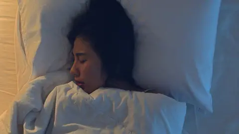 Nervous young Asian woman having a nightmare lying on bed in her bedroom at home in middle of night. Suffering from headache or migraine, Insomnia, sleep apnea or stress concept. Top view shot.