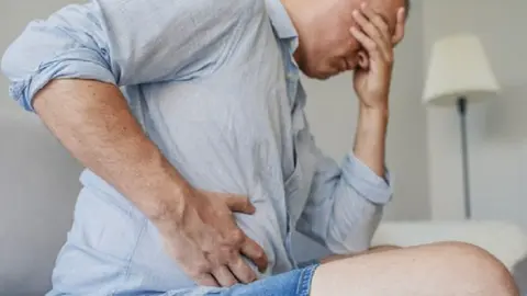 Terrible stomachache. Frustrated handsome young man hugging his belly and keeping eyes closed. Disturbed male having pain in stomach