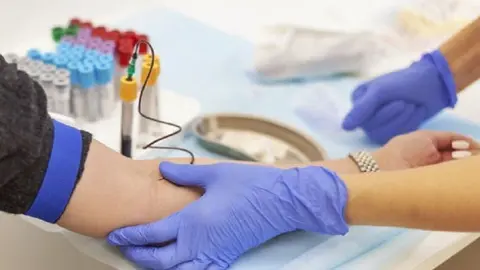 A doctor in blue gloves takes blood from a vein from a young woman. Several test tubes. Diagnosis, disease, examination concept.