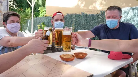 People with face masks cheering with beers in a bar. New normality in bars concept.