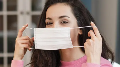 Mujer poni&eacute;ndose una mascarilla | Foto de archivo