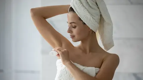 Una mujer aplicando desodorante en las axilas