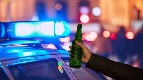 Una persona con una botella junto a un coche de Polic&iacute;a
