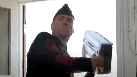 El Sargento Flamenco tira un radio cassette con m&uacute;sica reguetonera.