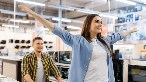 Happy family couple with cart in electronics store. Man and woman buying home electrical appliances in market