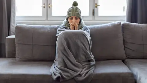 Mujer tiembla de fr&iacute;o en el sof&aacute; de su casa