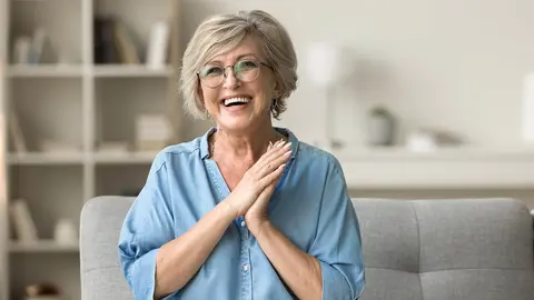 Mujer de edad media alegre sentada en el sof&aacute; de su casa