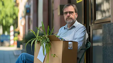 Hombre despedido del trabajo se muestra cabizbajo sentado en un banco con su caja de enseres