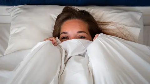 Mujer mirando por encima de la funda n&oacute;rdica de su cama