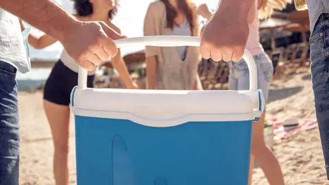 Ba&ntilde;istas cargan juntos en peso la nevera en la playa