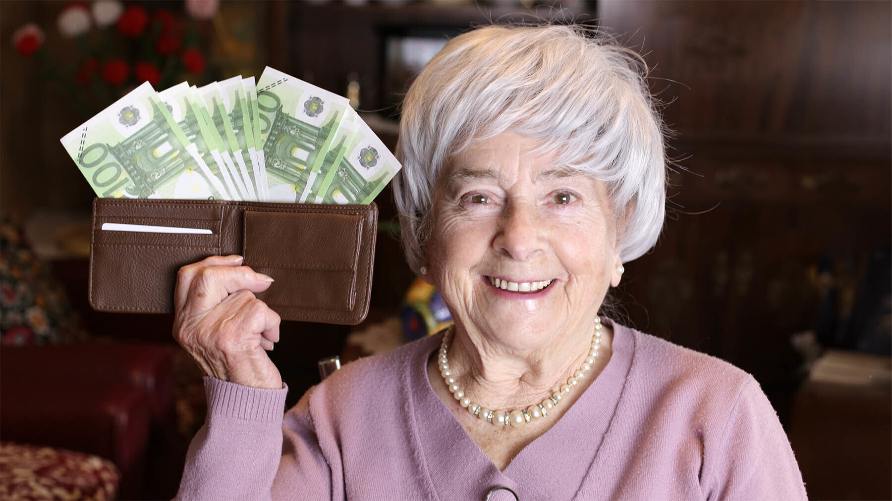 Mujer pensionista sostiene una cartera llena de billetes de 100 euros