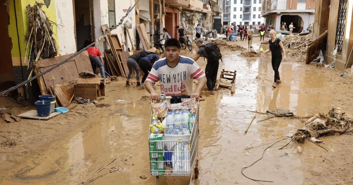 Un vecino de Paiporta traslada alimentos mientras otros limpian una calle afectada